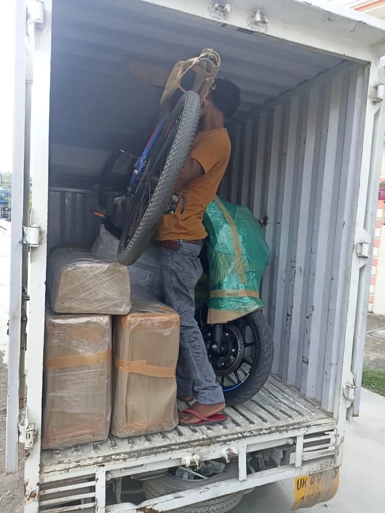 Agarwal Packers and Movers worker loading sealed cartons and a wrapped two-wheeler into a transport truck in Dehradun